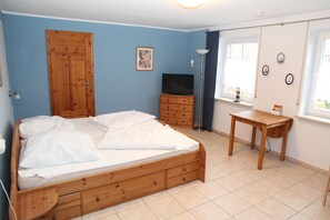 Une chambre à coucher avec un lit en bois, une télévision, un bureau et une fenêtre avec des rideaux.