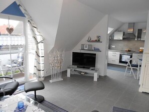 A modern kitchen with a built-in oven and microwave, a dining area with a glass table and chairs, and a living room with a TV and decorative plants.
