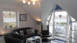 Una sala de estar moderna con un sofá negro, una mesita de centro pequeña, un sillón negro y un ventanal con vistas al exterior.