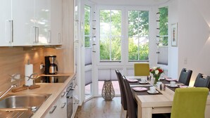 A modern kitchen with white cabinets, a wooden countertop, and a dining area with a table set for four. - Sehr Schöne Ferienwohnung in Zentraler und Ruhiger Lage (Greetsiel)