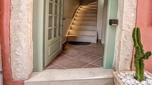 Eine Treppe führt zu einer oberen Etage, eine Tür mit Fensterfeldern und eine Kakteenpflanze in einem Blumentopf.