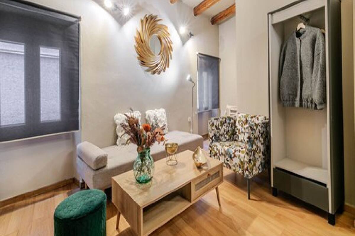 Un salon moderne avec un canapé, une table basse et un fauteuil à motifs. On y trouve également un porte-manteau sur lequel est accrochée une veste.