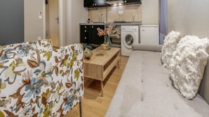 Ein kompakter Wohnraum mit Küchenzeile, einer Waschmaschine, einem Holztisch und einem Sofa.