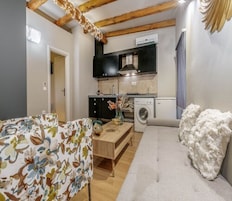 A compact living space with a kitchenette, a washing machine, a wooden dining table, and a sofa.