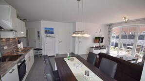 A modern kitchen with a dining area, a view of the outside, and a large window. - Erdgeschosswohnung "godewind" Zentral in Greetsiel (Greetsiel)