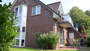 A two-story brick house with a covered patio, a window, and a door. - Erdgeschosswohnung "godewind" Zentral in Greetsiel (Greetsiel)