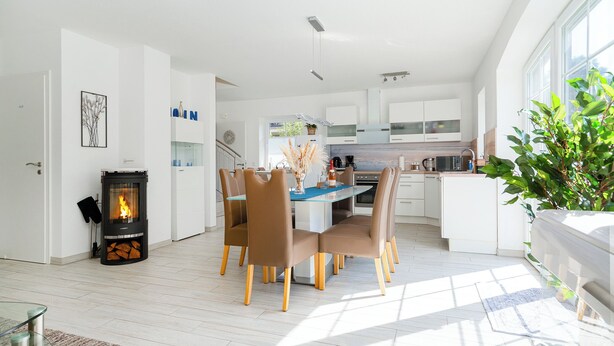 Una cucina moderna con mobili bianchi, un'isola centrale e un'area pranzo con sedie marroni.