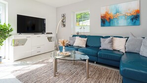 Un soggiorno moderno con un tavolino in vetro, un divano blu, un televisore a schermo piatto e un grande quadro astratto appeso al muro.