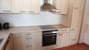 Une cuisine avec des meubles de couleur bois clair, une hotte de cuisinière en acier inoxydable, un four encastré et une machine à café posée sur le plan de travail.
