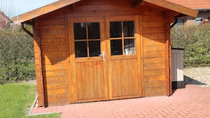 Une cabane en bois avec une grande porte et des fenêtres en bois, un chemin pavé de briques et un toit recouvert de tuiles rouges.