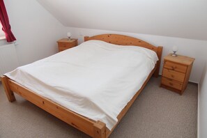 Ein Einzelbett mit Holzrahmen und weißer Bettwäsche in einem Raum mit schrägem Dach. Zwei Nachttische aus Holz mit Lampen sind vorhanden, und eine Heizung ist an der Wand sichtbar.