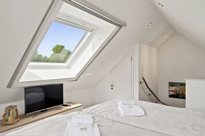 Ein Schlafzimmer mit Dachfenster, einem Bett, einem Fernseher und einem Bild an der Wand.
