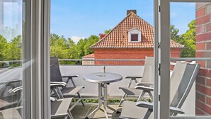 A balcony with a table and chairs, a red brick building in the background, and a clear blue sky. - Wunderschöne Ferienwohnung im Ortskern (Greetsiel)