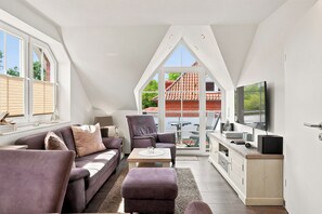 A modern loft apartment with a high ceiling, large windows, a flat-screen TV, and a cozy seating area. - Wunderschöne Ferienwohnung im Ortskern (Greetsiel)