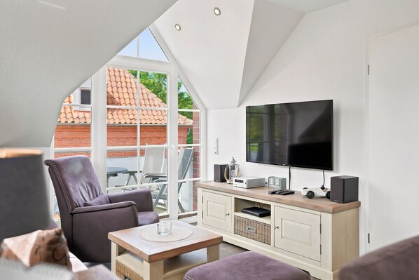 Ein modernes Wohnzimmer mit Fernseher, Sitzgelegenheiten und Blick durch ein großes Fenster.