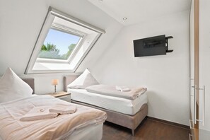 Ein Schlafzimmer mit Dachfenster, einem Bett, einem Nachttisch mit Lampe und einem an der Wand befestigten Fernseher.