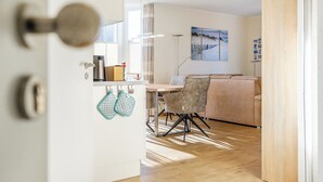 A modern kitchen with a dining area, featuring a wooden floor, a grey sofa, and a painting on the wall. - Schöne Ferienwohnung in Wassernähe (Greetsiel)