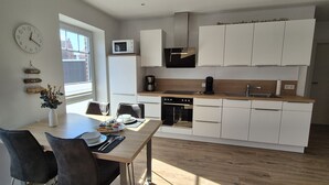 Een moderne keuken met witte kasten, een magnetron, een koffiezetapparaat en een eethoek met een tafel en stoelen.