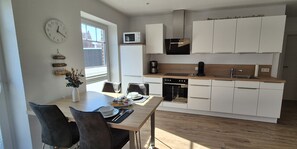 Une cuisine moderne avec des meubles blancs, un four à micro-ondes, une machine à café et un coin repas comprenant une table et des chaises.