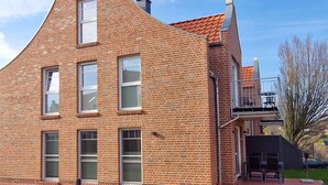 Een gebouw van baksteen met een uniek gebogen dak, meerdere ramen en een geplaveid gebied met een hek ervoor.