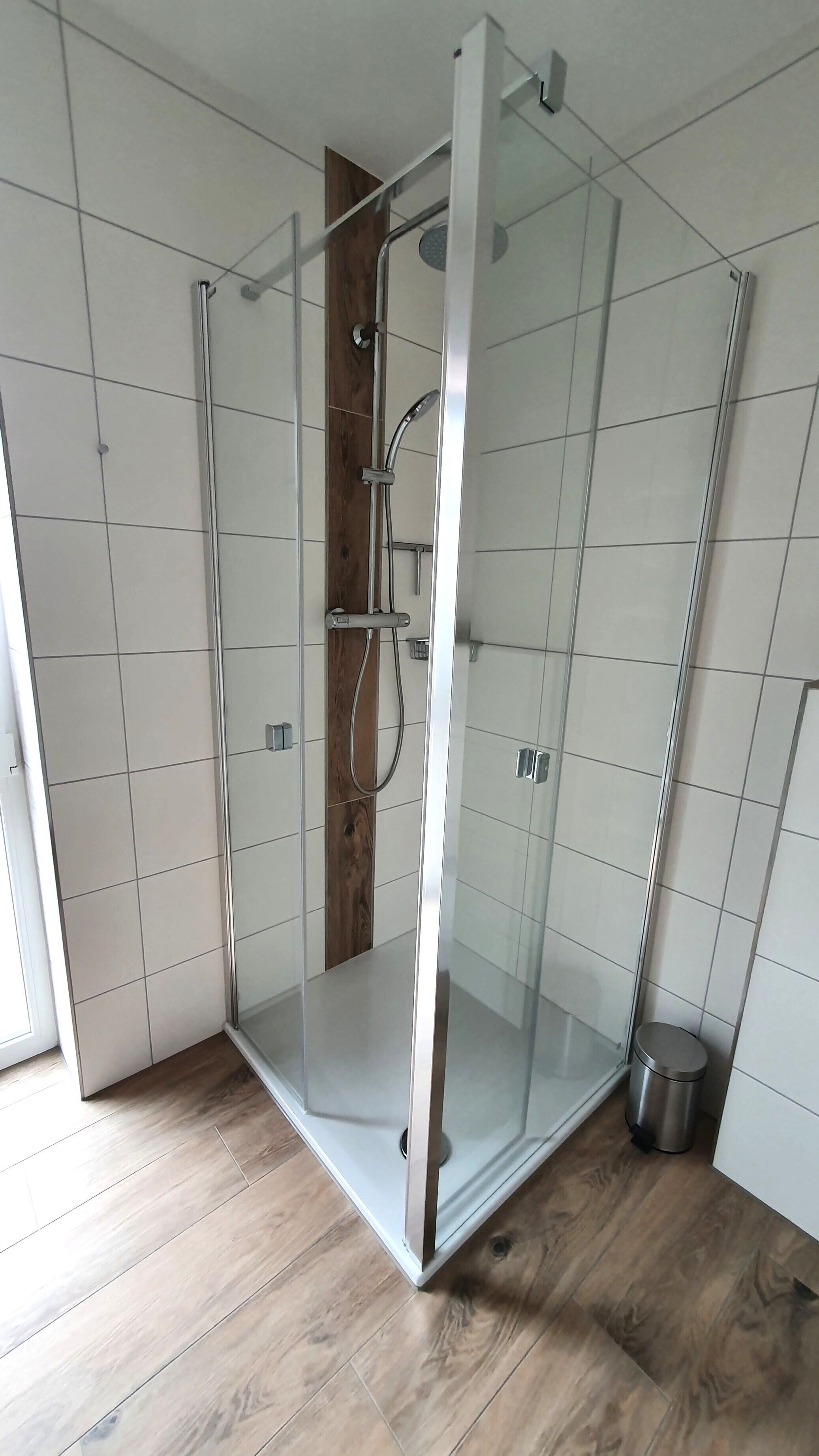 Une douche entièrementClose avec des parois en verre, un plancher en bois et des murs carrelés.