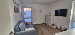 Un espace de vie compact comprenant un canapé, un téléviseur, une petite table et un meuble.