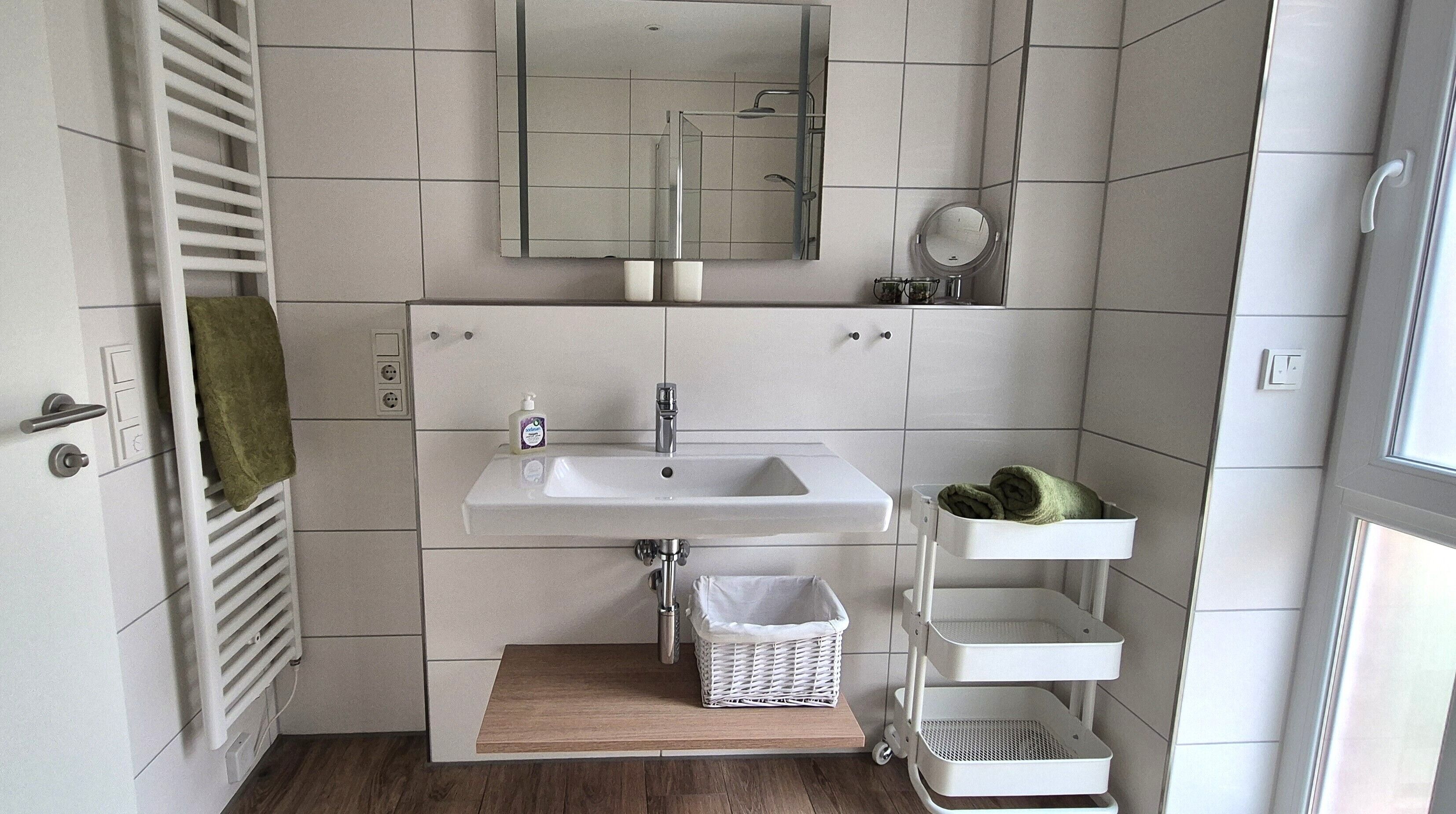 Een badkamer met een witte wastafel, spiegel, handdoekrek en een klein houten plankje.
