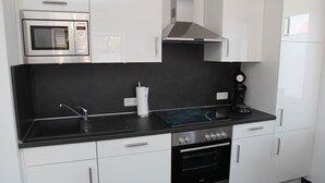 A modern kitchen with white cabinets, a black countertop, a built-in microwave, a stove, and a coffee maker. - Zentral Gelegene Ferienwohnung in Greetsiel (Greetsiel)
