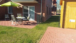 A patio with a table and chairs, a green umbrella, and a brick wall. - Zentral Gelegene Ferienwohnung in Greetsiel (Greetsiel)