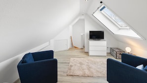Un dormitorio estilo loft moderno con tragaluces, un televisor y dos sillones azules.