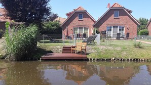 A riverside view with a wooden deck, a bench, and a brick house with a satellite dish.