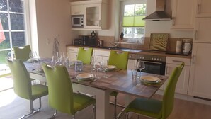 A modern kitchen with white cabinets, a wooden countertop, and a dining area with green chairs and a wooden table set for four.