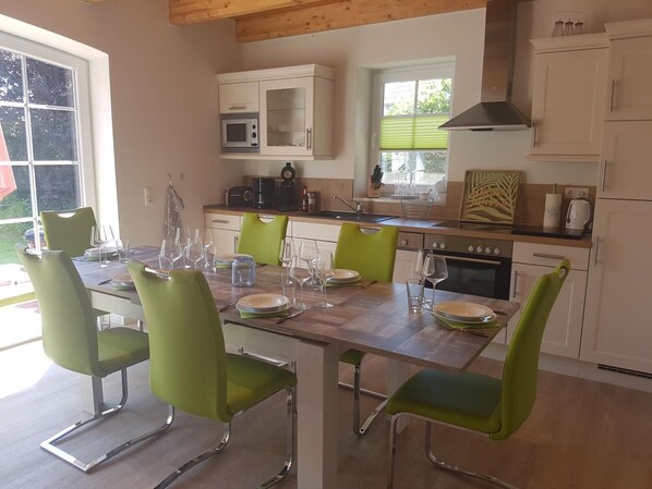 Une cuisine moderne avec des meubles blancs, un plan de travail en bois et un coin repas comprenant des chaises vertes et une table en bois, le tout disposé pour accueillir quatre personnes.