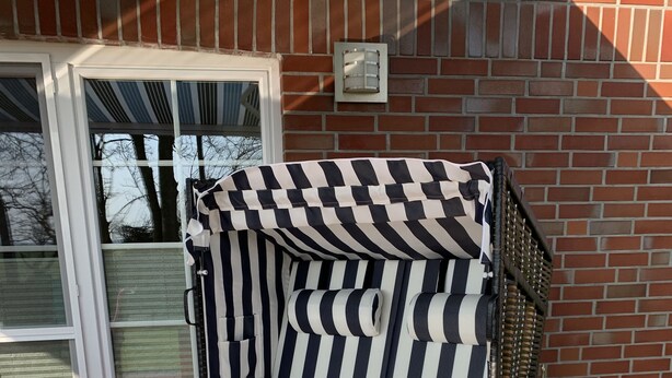 A striped outdoor chair with a wooden frame and a metal grill, placed on a brick patio. - Allergikerfreundliches Ferienhaus in Hilgenriedersiel (Hilgenriedersiel-Hagermarsch)