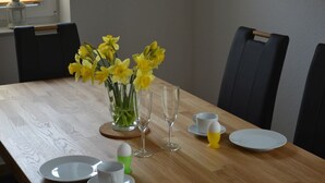 A dining table set with a vase of yellow flowers, wine glasses, and plates. - Allergikerfreundliches Ferienhaus in Hilgenriedersiel (Hilgenriedersiel-Hagermarsch)