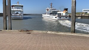 Two boats on a calm waterway, wooden posts on the left, and a paved walkway in the foreground. - Allergikerfreundliches Ferienhaus in Hilgenriedersiel (Hilgenriedersiel-Hagermarsch)