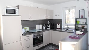 A modern kitchen with white cabinets, a microwave, a coffee maker, and a sink. - Ferienhaus mit Traumhaftem Seeblick (Warin)