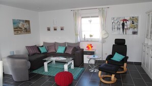 A modern living room with a sofa, two chairs, a coffee table, and a red knitted pouf. - Ferienhaus mit Traumhaftem Seeblick (Warin)