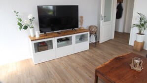 Una sala de estar moderna con un televisor de pantalla plana sobre un mueble bajo de madera, armarios blancos y una mesa de centro de madera.