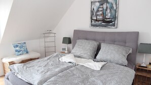 Un dormitorio con una cama grande, una mesita de noche, una lámpara, una pequeña mesa con lámpara, una silla, un reloj de pared y un cuadro.