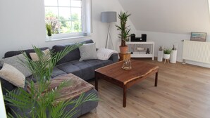 Una sala de estar moderna con un sofá gris, una mesa de centro de madera y un ventanal con persianas.