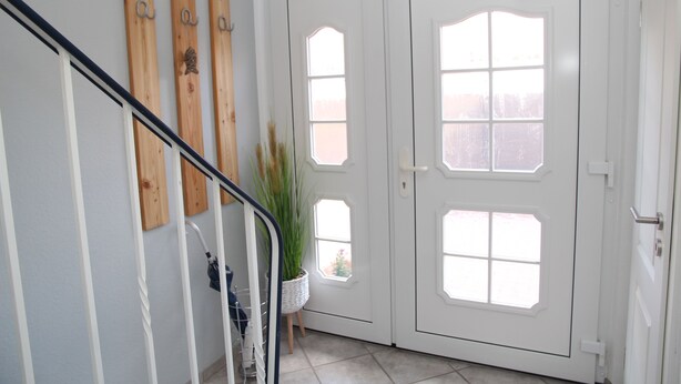 Una escalera con barandilla, decoraciones de madera en la pared, una planta en maceta y una puerta blanca con paneles de vidrio.