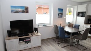A modern kitchen with a flat-screen TV, dining table, and chairs.