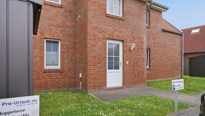 A red brick house with a white door and windows, a small front yard with grass and flowers, and a sign indicating parking availability.