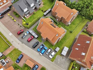 Vista aérea de una zona residencial con varias casas, un estacionamiento con varios coches y una calle despejada con un cartel de límite de velocidad.