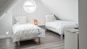 Une chambre avec deux lits, une fenêtre ronde et une petite table.