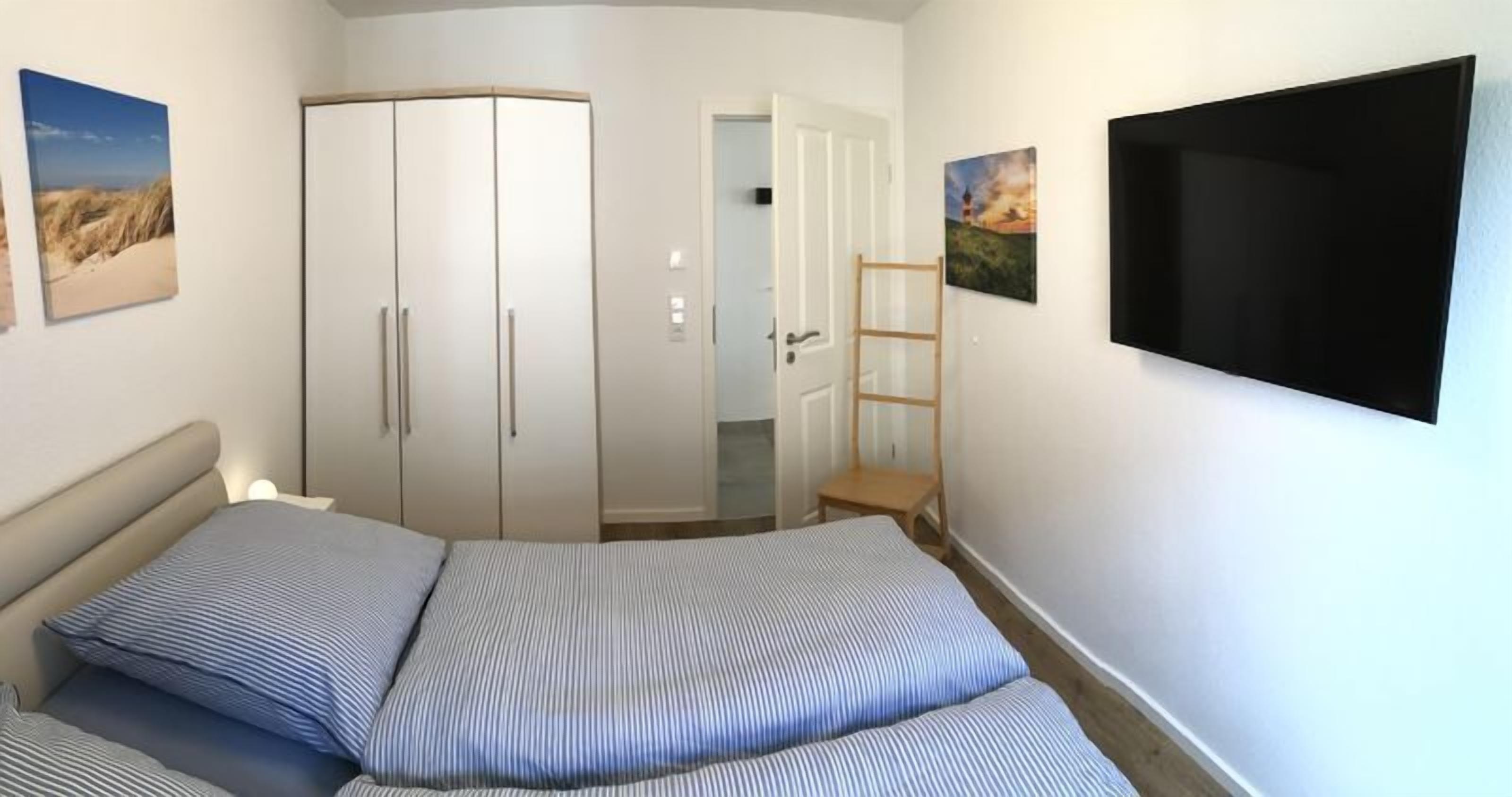 A bedroom with a bed, a wardrobe, a TV, and artwork on the walls.