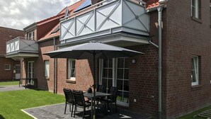En patio med et bord og stole, et overdækket opholdsområde og en murbygning med rødt tag.