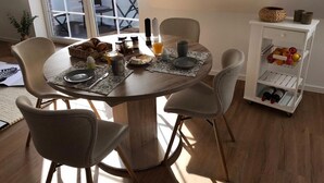 Een eethoek met een ronde tafel, vier stoelen, een klein plankje met flessen, en een raam met uitzicht op het omliggende landschap.