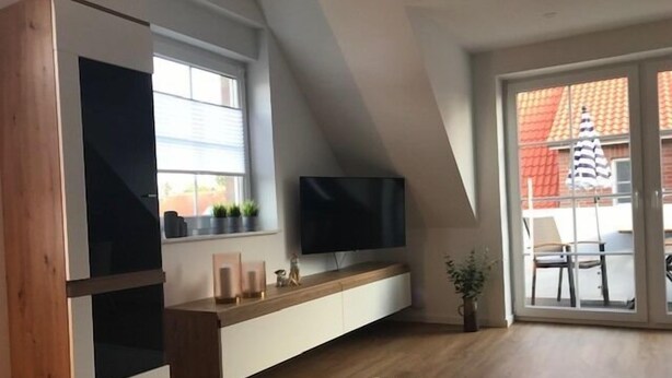 Een moderne woonkamer met een tv op een houten console, een groot raam en een schuifdeur naar een buitenruimte.